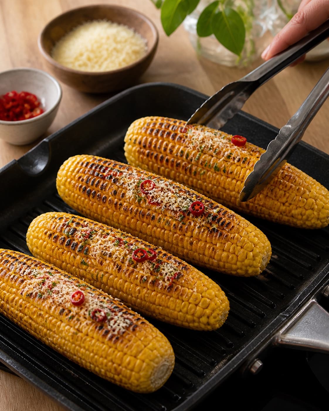 One single photorealistic instructional frame of the main ingredient grilling with clear sear marks for Majskolber med parmesan og chili, featuring majskolber, parmesan, chili, with only the named equipment and no unrelated food, text, logos or packaging under tilberedningen af majskolber med parmesan og chili