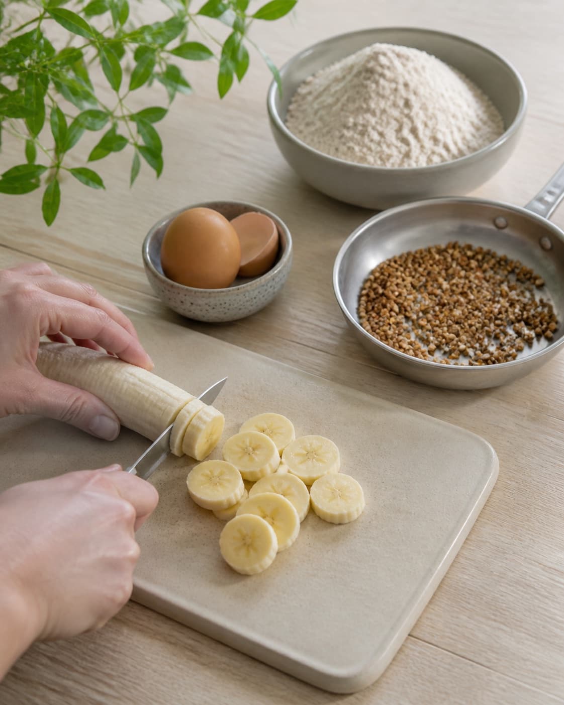 One single photorealistic instructional frame of fresh fruit being cut beside one small pan of toasted topping for Morgenmadsvafler med boghvede, featuring boghvedemel, banan, æg, with only the named equipment and no unrelated food, text, logos or packaging under tilberedningen af morgenmadsvafler med boghvede