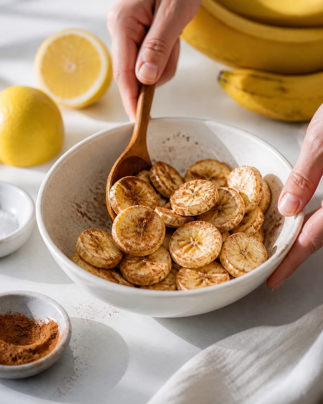 One single photorealistic instructional frame of the main ingredient being evenly coated with seasoning for Bananchips, featuring bananer, citron, stødt kanel, with only the named equipment and no unrelated food, text, logos or packaging under tilberedningen af bananchips