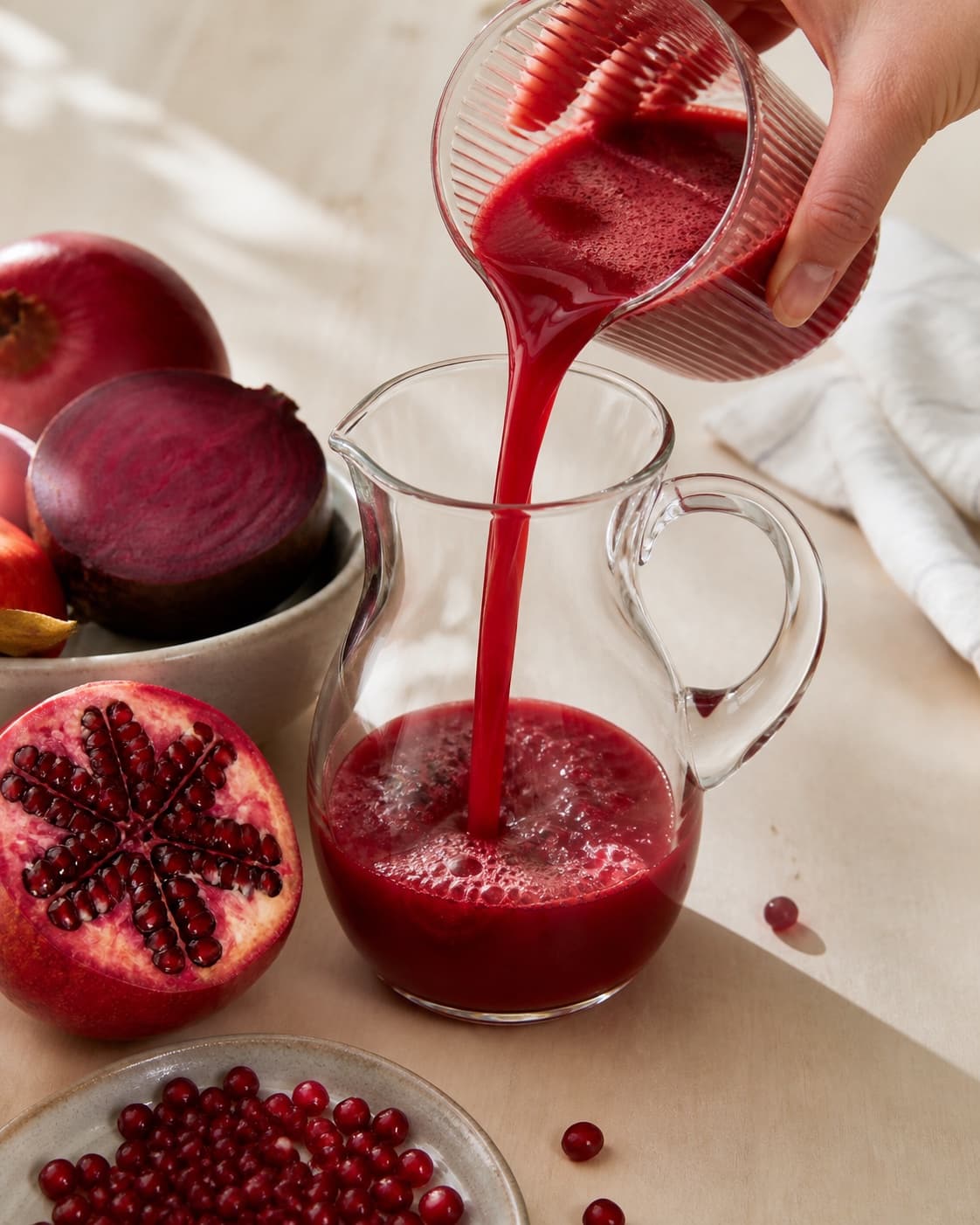 One single photorealistic instructional frame of colorful fresh juice flowing into one clean jug for Granatæble juice med power, featuring granatæblekerner, æbler, rødbede, with only the named equipment and no unrelated food, text, logos or packaging under tilberedningen af granatæble juice med power