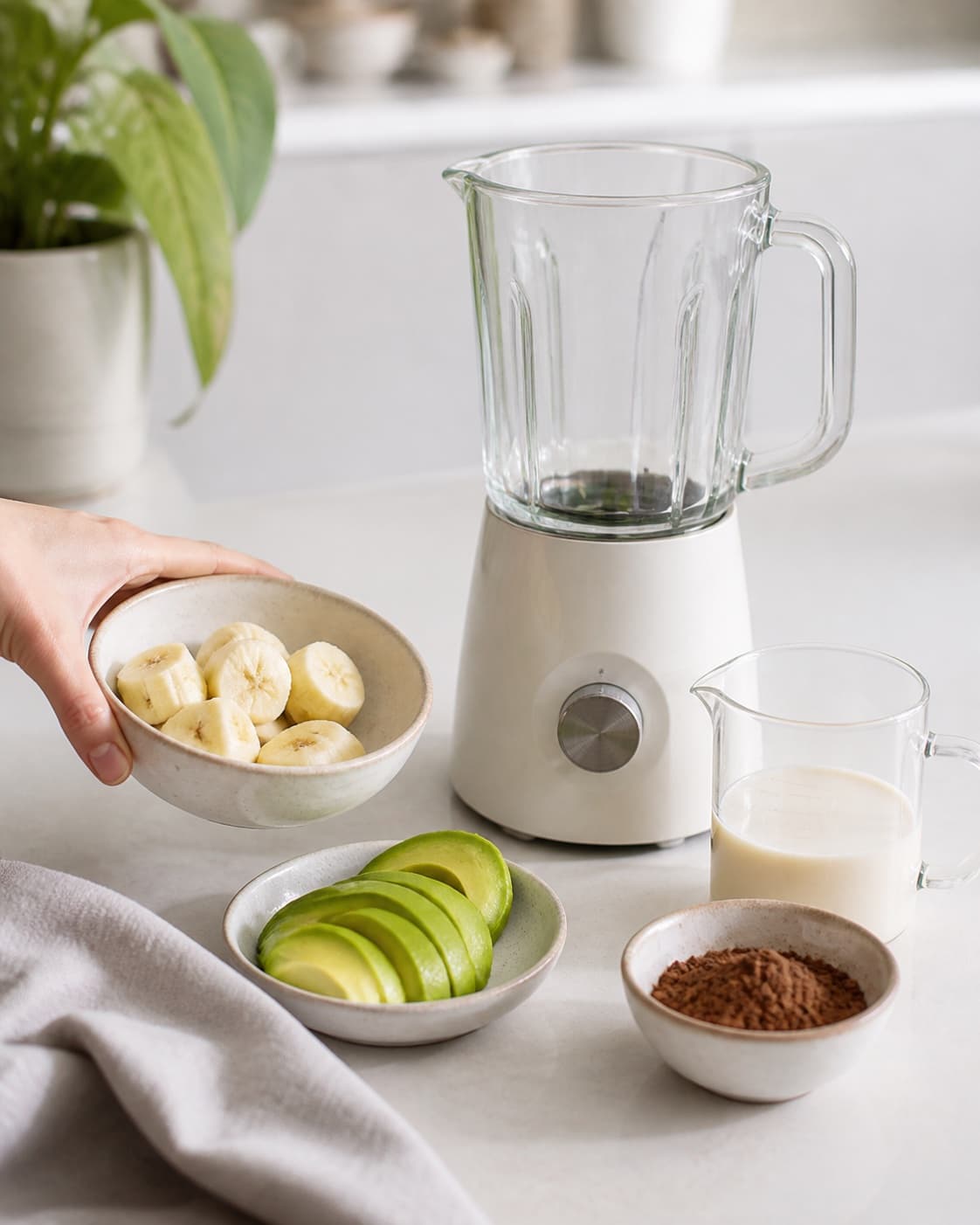 One single photorealistic instructional frame of prepared fruit and measured liquid beside one blender for Sund Chokolade Smoothie, featuring banan, kakaopulver, avocado, with only the named equipment and no unrelated food, text, logos or packaging under tilberedningen af sund chokolade smoothie