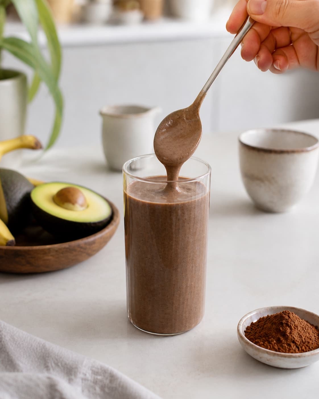 One single photorealistic instructional frame of one spoon checking the thick smoothie consistency for Sund Chokolade Smoothie, featuring banan, kakaopulver, avocado, with only the named equipment and no unrelated food, text, logos or packaging under tilberedningen af sund chokolade smoothie