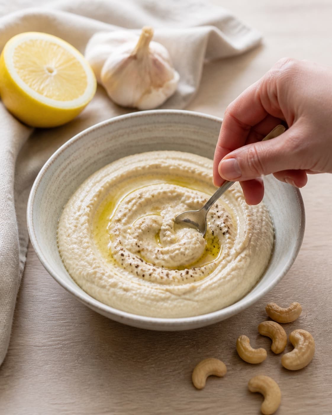 One single photorealistic instructional frame of one bowl of finished dip being tasted and adjusted for Cashewnød dip, featuring cashewnødder, citron, hvidløg, with only the named equipment and no unrelated food, text, logos or packaging under tilberedningen af cashewnød dip