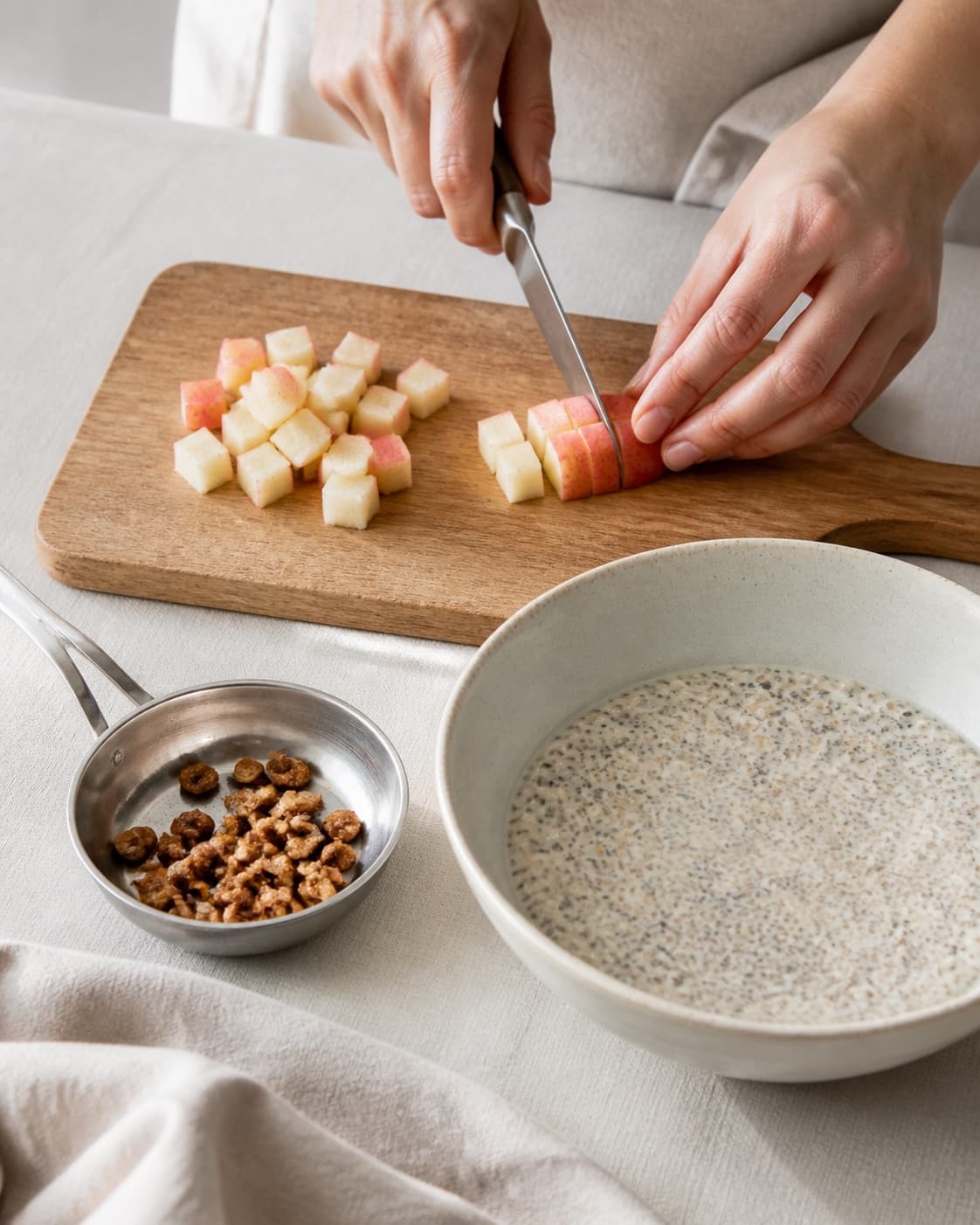 One single photorealistic instructional frame of fresh fruit being cut beside one small pan of toasted topping for Køleskabsgrød, featuring havregryn, mælk, chiafrø, with only the named equipment and no unrelated food, text, logos or packaging under tilberedningen af køleskabsgrød