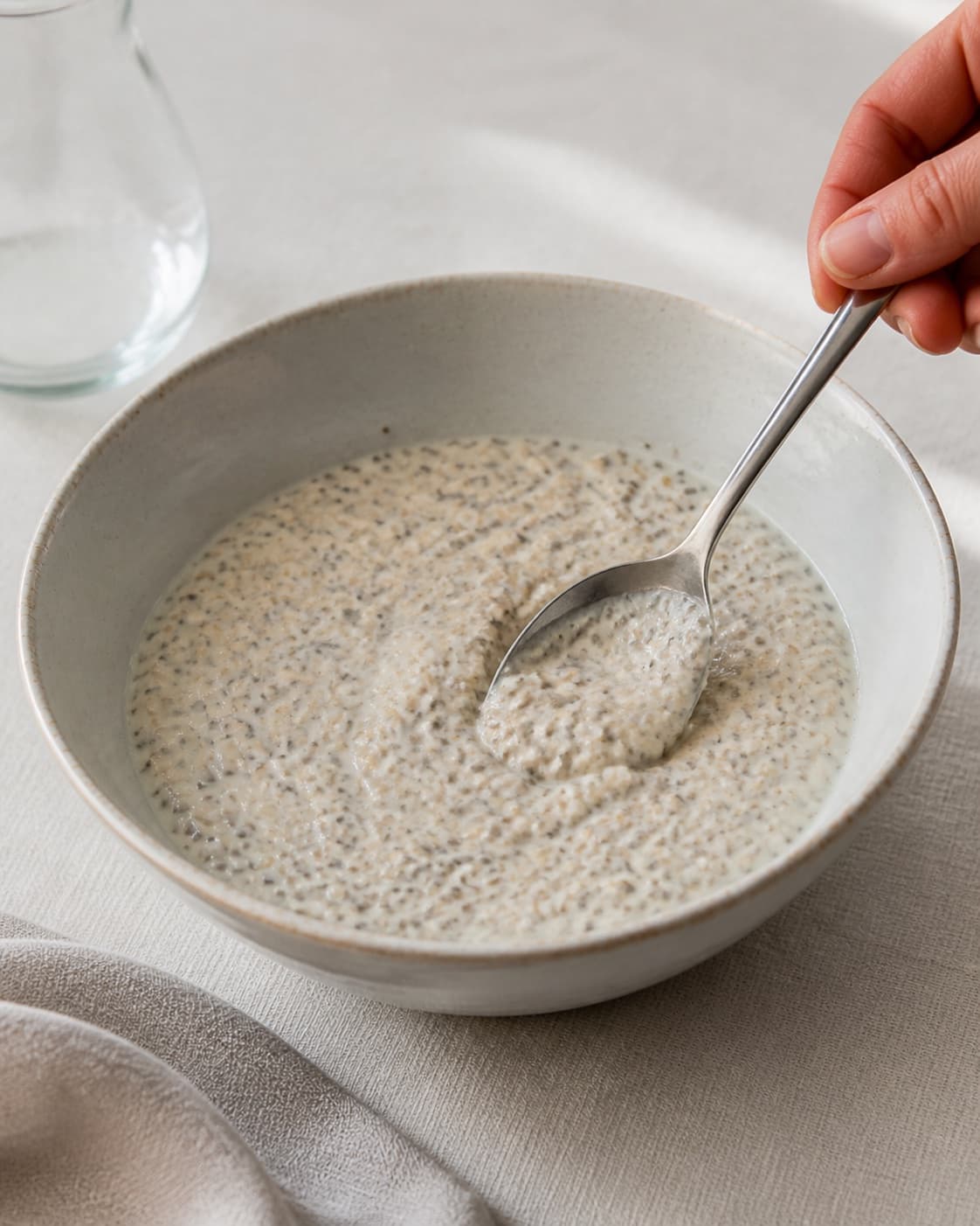 One single photorealistic instructional frame of the porridge consistency being adjusted with a spoon for Køleskabsgrød, featuring havregryn, mælk, chiafrø, with only the named equipment and no unrelated food, text, logos or packaging under tilberedningen af køleskabsgrød