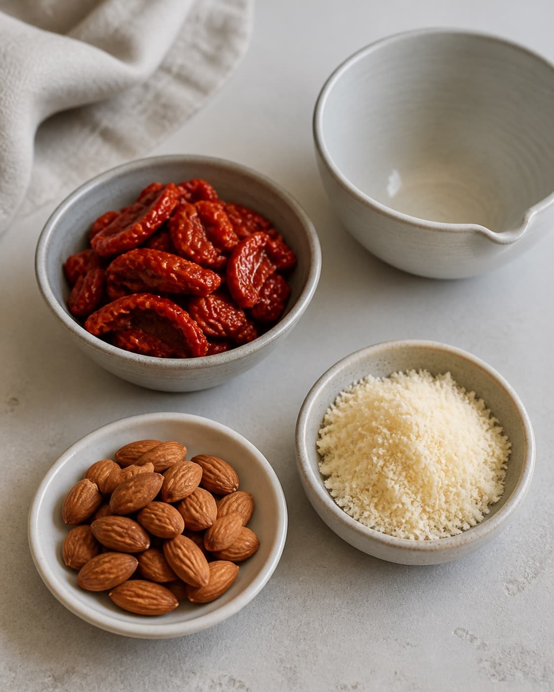 One single photorealistic instructional frame of the dip ingredients measured in separate small bowls for Tomatpesto, featuring soltørrede tomater, parmesan, mandler, with only the named equipment and no unrelated food, text, logos or packaging under tilberedningen af tomatpesto