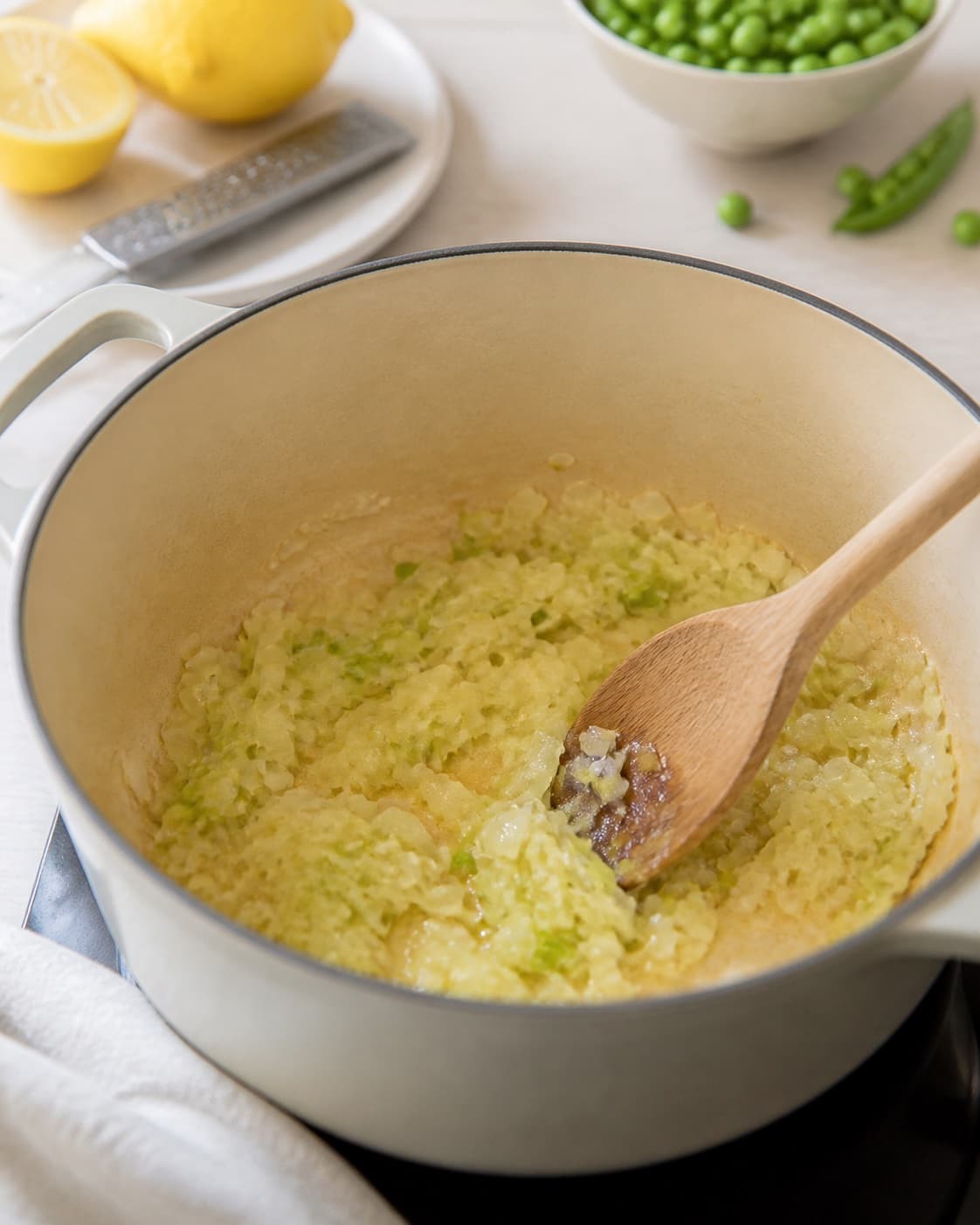 One single photorealistic instructional frame of aromatic vegetables softening in the same heavy pot for Pasta med ærter og citron, featuring pasta, grønne ærter, citron, with only the named equipment and no unrelated food, text, logos or packaging under tilberedningen af pasta med ærter og citron