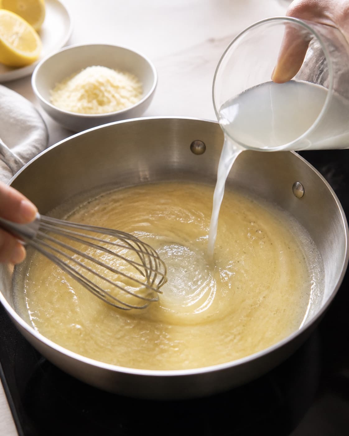 A pale glossy lemon parmesan sauce being emulsified with pasta water in one pan, no brown stock or meat under tilberedningen af pasta med ærter og citron