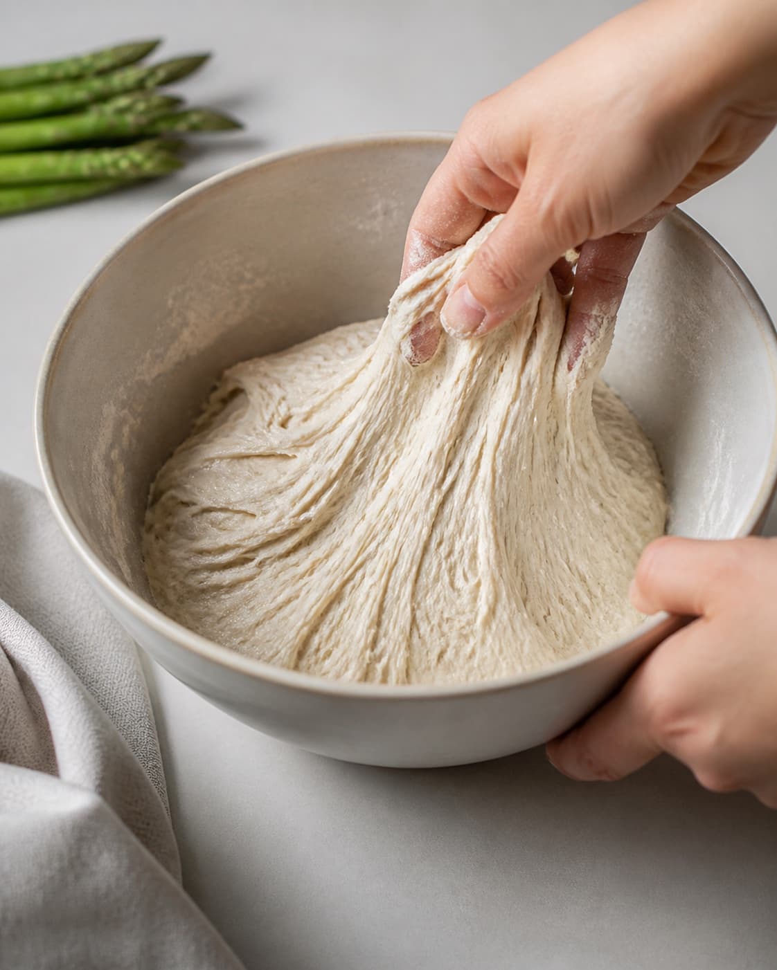 One single photorealistic instructional frame of elastic pizza dough mixing in one bowl for Mini pizza med asparges, featuring hvedemel, gær, grønne asparges, with only the named equipment and no unrelated food, text, logos or packaging under tilberedningen af mini pizza med asparges