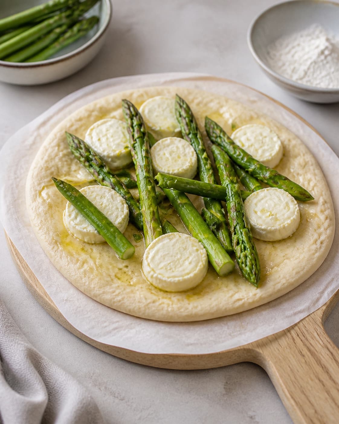 One single photorealistic instructional frame of the raw pizza shaped and topped before baking for Mini pizza med asparges, featuring hvedemel, gær, grønne asparges, with only the named equipment and no unrelated food, text, logos or packaging under tilberedningen af mini pizza med asparges
