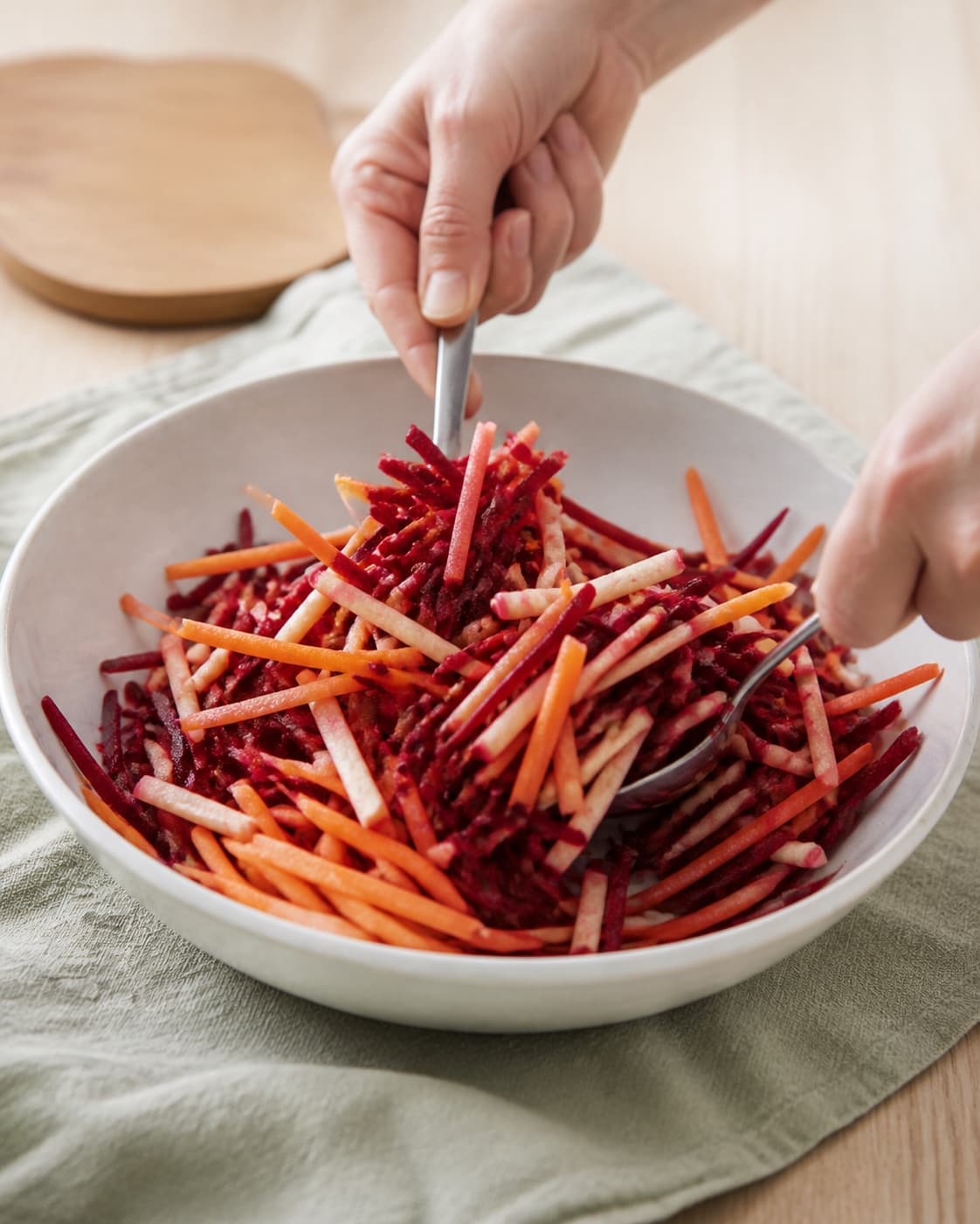 One single photorealistic instructional frame of the prepared salad components being gently tossed together for Råkost med rødbede, featuring rødbede, gulerødder, æble, with only the named equipment and no unrelated food, text, logos or packaging under tilberedningen af råkost med rødbede