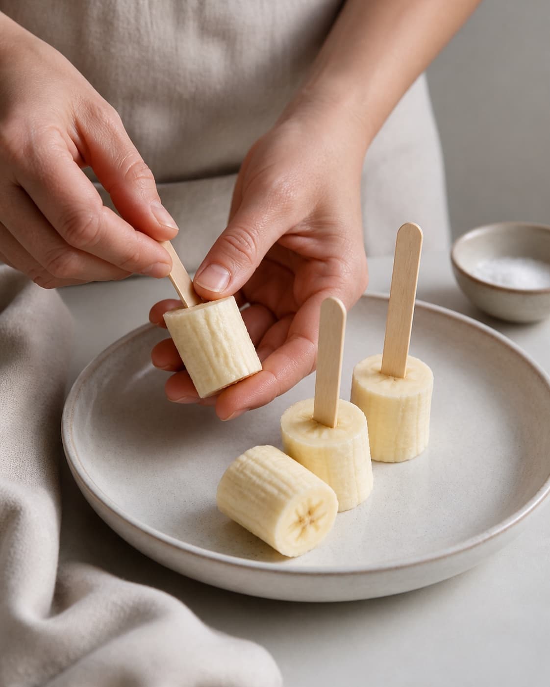 Wooden ice-pop sticks being inserted into fresh banana chunks, no custard or saucepan under tilberedningen af bananis af frosne bananstykker