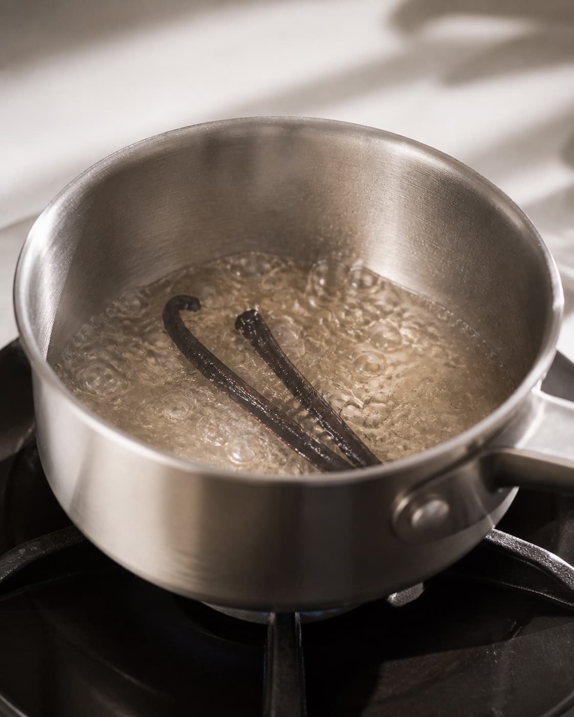 One single photorealistic instructional frame of the sauce base simmering in one saucepan for Vaniljesirup, featuring sukker, vand, vaniljestang, with only the named equipment and no unrelated food, text, logos or packaging under tilberedningen af vaniljesirup