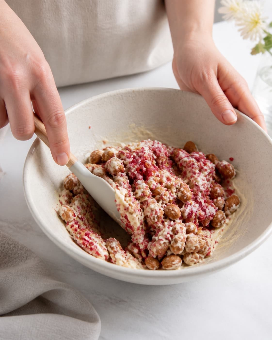 One single photorealistic instructional frame of the flavoring being folded into the confection mixture for Mandler med hvid chokolade og hindbærdrys, featuring mandler, hvid chokolade, frysetørrede hindbær, with only the named equipment and no unrelated food, text, logos or packaging under tilberedningen af mandler med hvid chokolade og hindbærdrys
