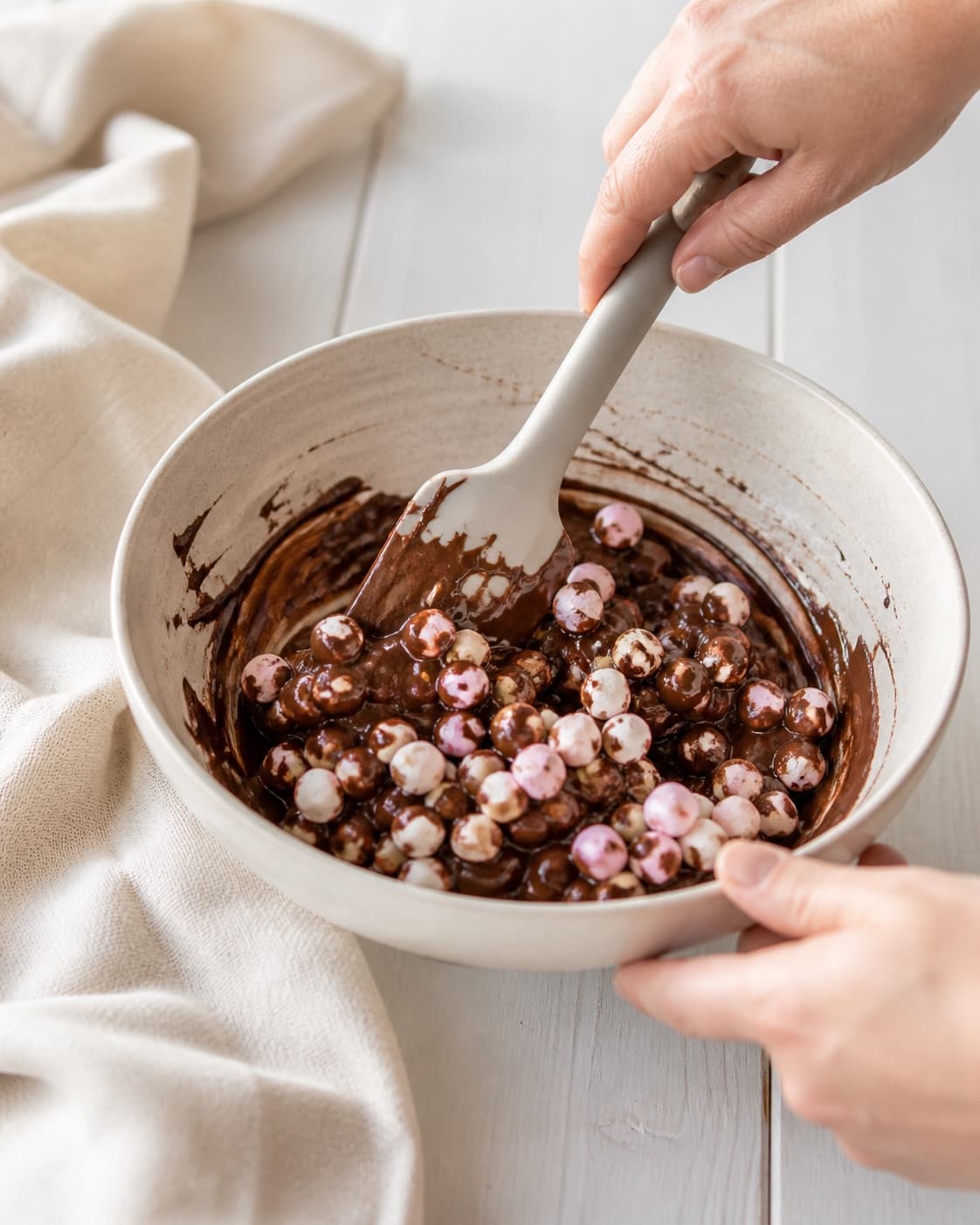 One single photorealistic instructional frame of the flavoring being folded into the confection mixture for Chokoladepinde, featuring mørk chokolade, skumfiduser, hvid chokolade, with only the named equipment and no unrelated food, text, logos or packaging under tilberedningen af chokoladepinde