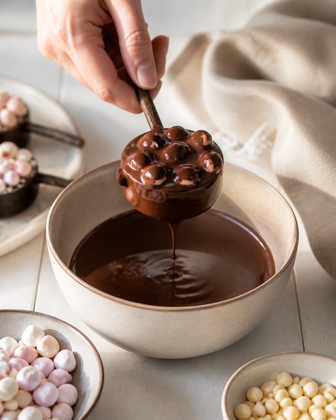 One single photorealistic instructional frame of the shaped pieces receiving an even coating for Chokoladepinde, featuring mørk chokolade, skumfiduser, hvid chokolade, with only the named equipment and no unrelated food, text, logos or packaging under tilberedningen af chokoladepinde