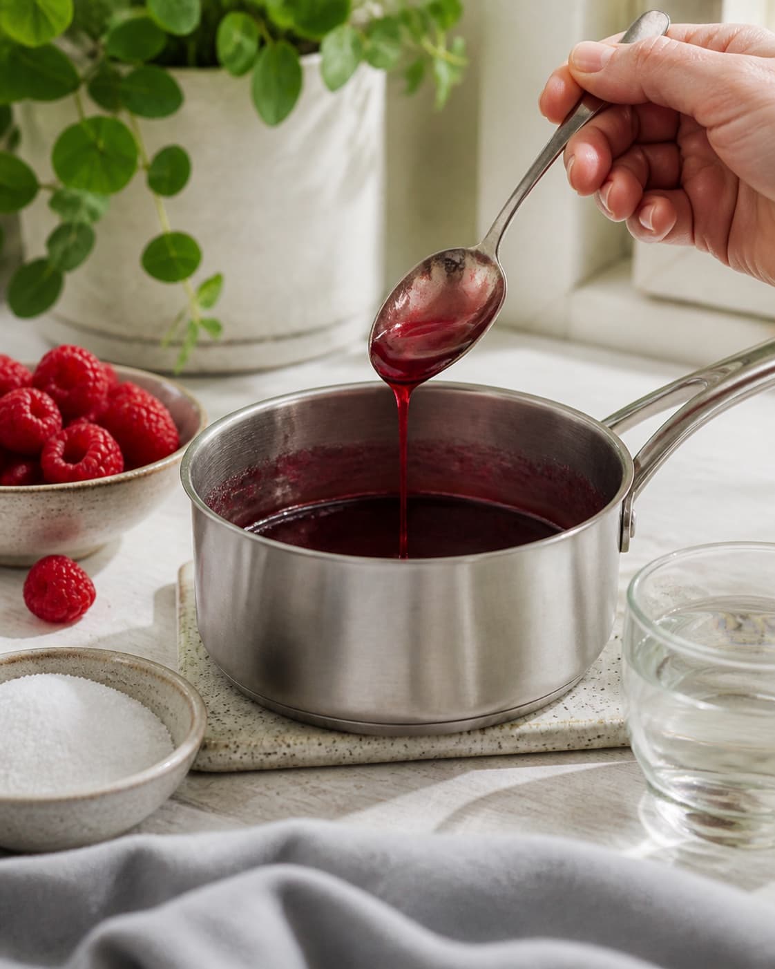 One single photorealistic instructional frame of the sauce consistency and seasoning being checked for Hindbærsirup med vanilje, featuring hindbær, sukker, vand, with only the named equipment and no unrelated food, text, logos or packaging under tilberedningen af hindbærsirup med vanilje