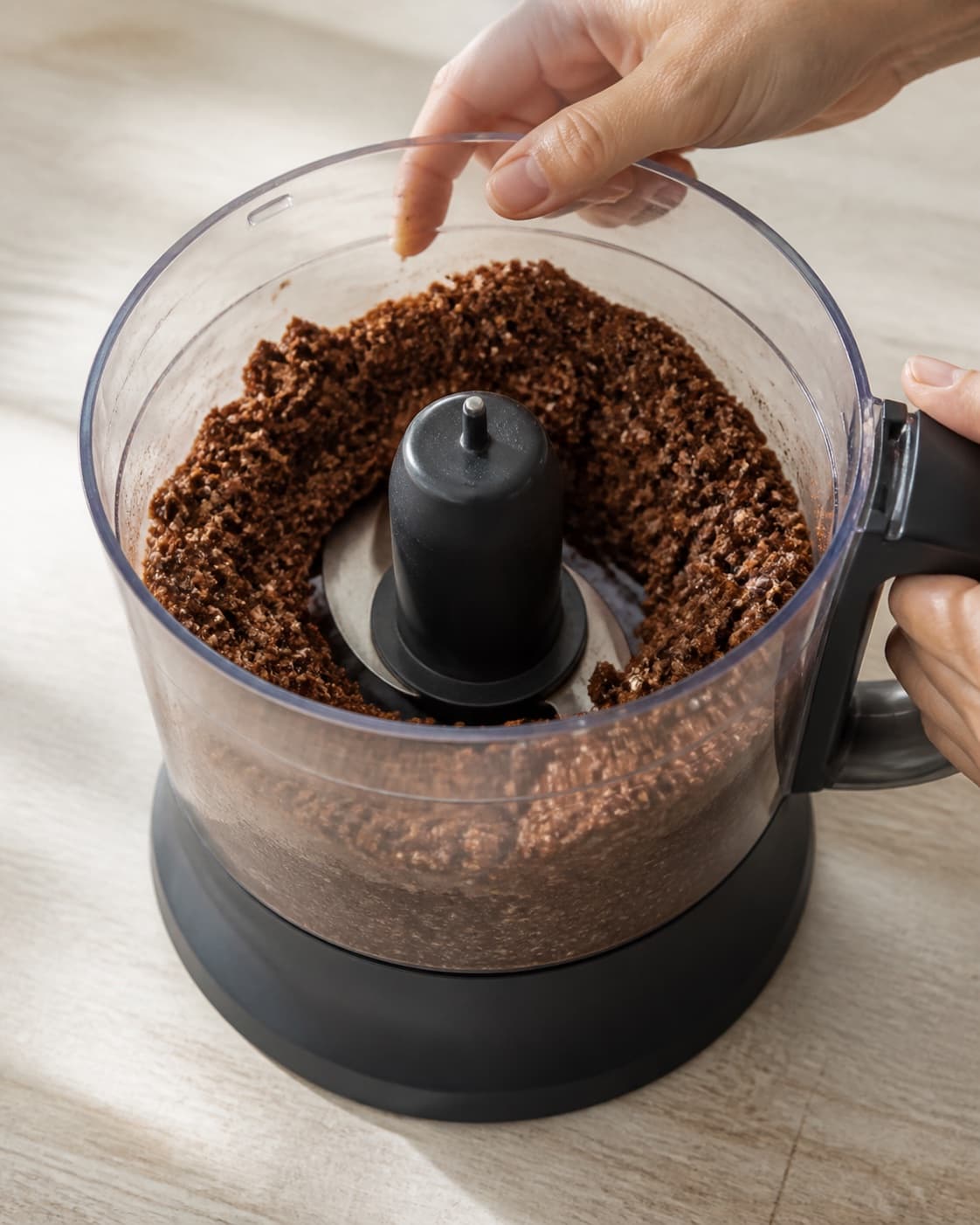 One single photorealistic instructional frame of the confection base becoming cohesive in one food processor for Sunde chokolade kugler, featuring dadler, kakaopulver, havregryn, with only the named equipment and no unrelated food, text, logos or packaging under tilberedningen af sunde chokolade kugler