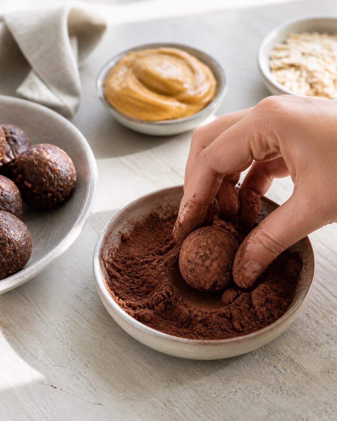 One single photorealistic instructional frame of the shaped pieces receiving an even coating for Sunde chokolade kugler, featuring dadler, kakaopulver, havregryn, with only the named equipment and no unrelated food, text, logos or packaging under tilberedningen af sunde chokolade kugler