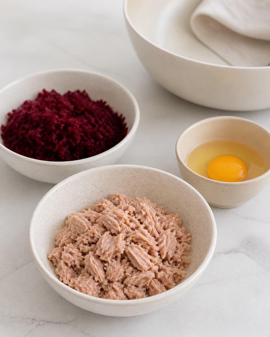 One single photorealistic instructional frame of finely prepared patty ingredients in separate bowls for Pink tundeller, featuring tun i vand, rødbede, æg, with only the named equipment and no unrelated food, text, logos or packaging under tilberedningen af pink tundeller