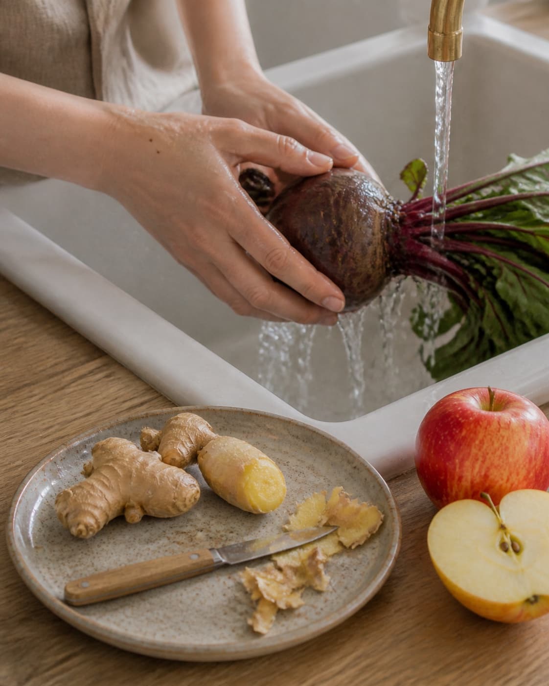 One single photorealistic instructional frame of fresh produce being washed and trimmed for Rødbedejuice med ingefær og æble, featuring rødbede, frisk ingefær, æble, with only the named equipment and no unrelated food, text, logos or packaging under tilberedningen af rødbedejuice med ingefær og æble