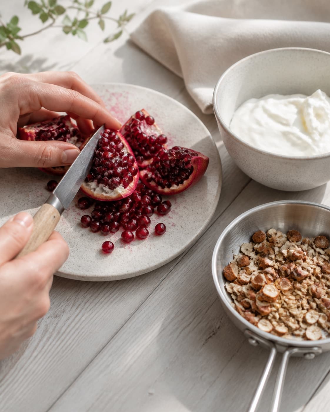 One single photorealistic instructional frame of fresh fruit being cut beside one small pan of toasted topping for Morgenmad med skyr og granatæble, featuring skyr, granatæblekerner, ristede mandler, with only the named equipment and no unrelated food, text, logos or packaging under tilberedningen af morgenmad med skyr og granatæble