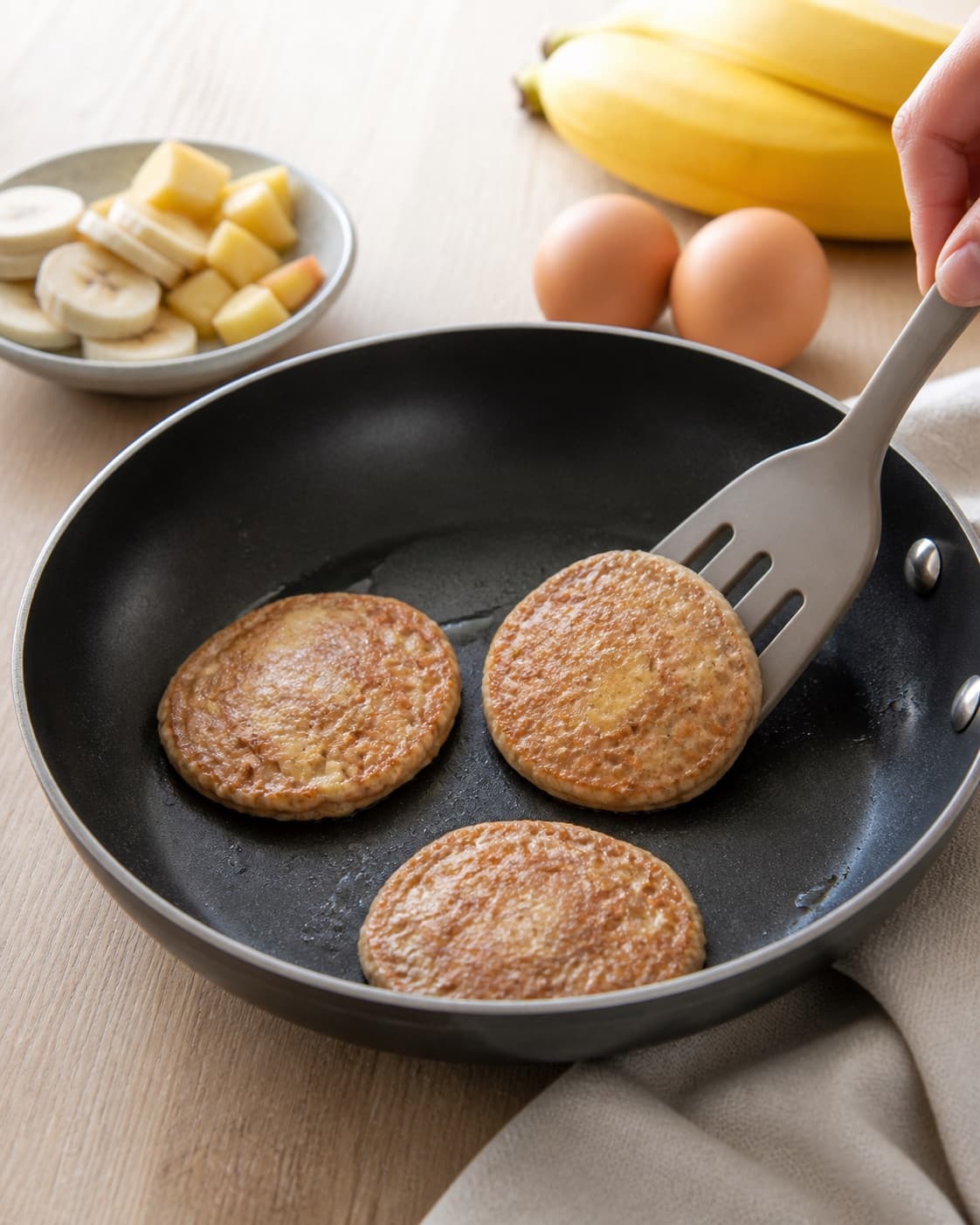 Small golden flourless banana and apple breakfast pancakes cooking in one skillet with a spatula, no saucepan or porridge under tilberedningen af morgenmadspandekager uden havregryn eller mel