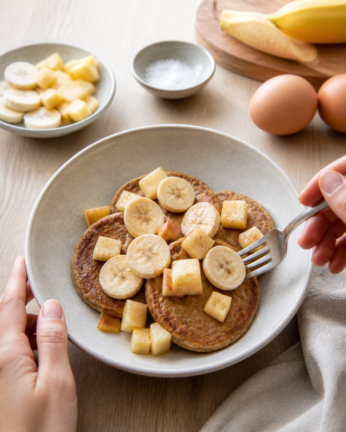 One single photorealistic instructional frame of finished breakfast bowls topped with the named fruit and garnish for Morgenmadspandekager uden havregryn eller mel, featuring banan, æg, æble, with only the named equipment and no unrelated food, text, logos or packaging under tilberedningen af morgenmadspandekager uden havregryn eller mel