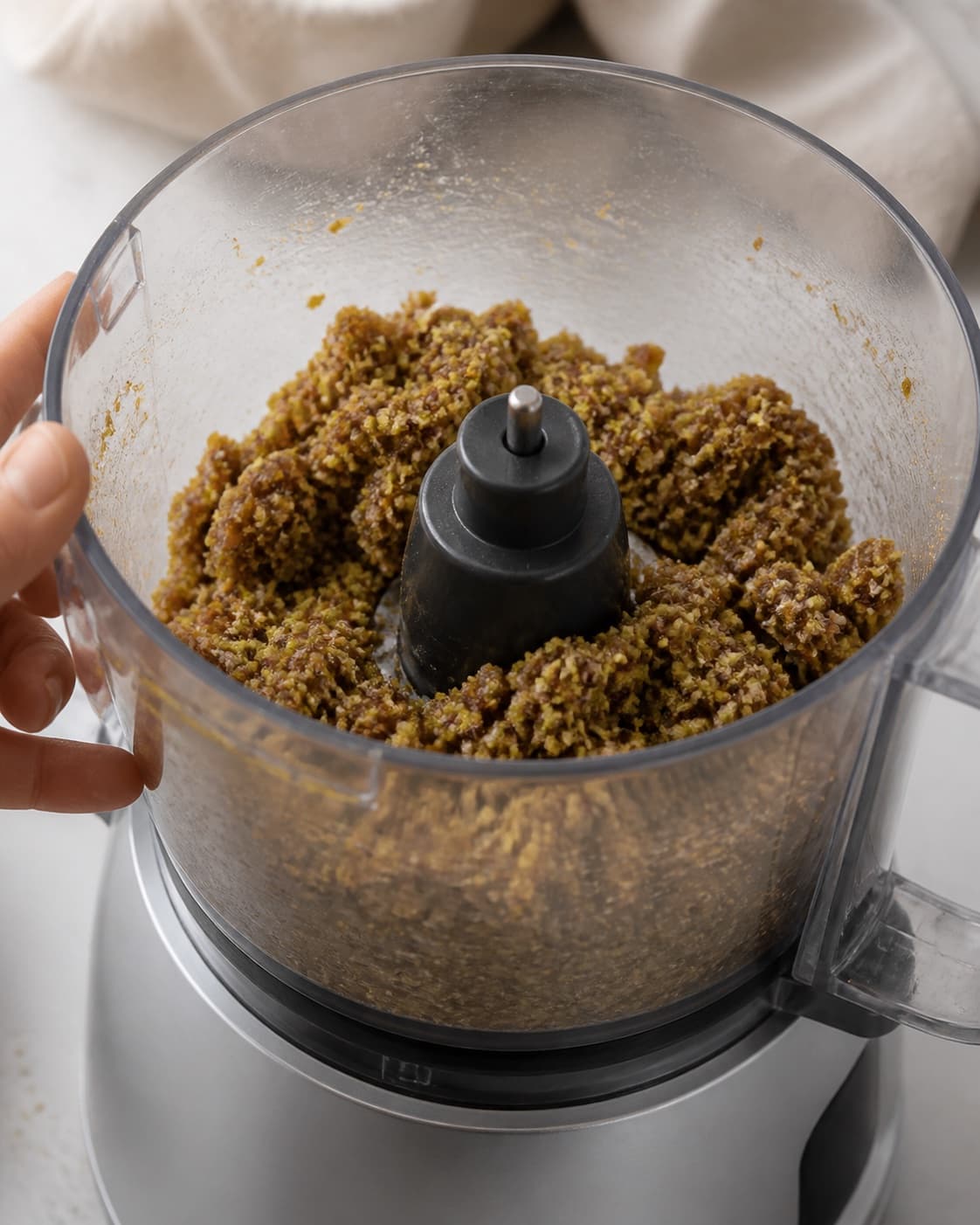 One single photorealistic instructional frame of the confection base becoming cohesive in one food processor for Figenkugler, featuring tørrede figner, dadler, pistacienødder, with only the named equipment and no unrelated food, text, logos or packaging under tilberedningen af figenkugler