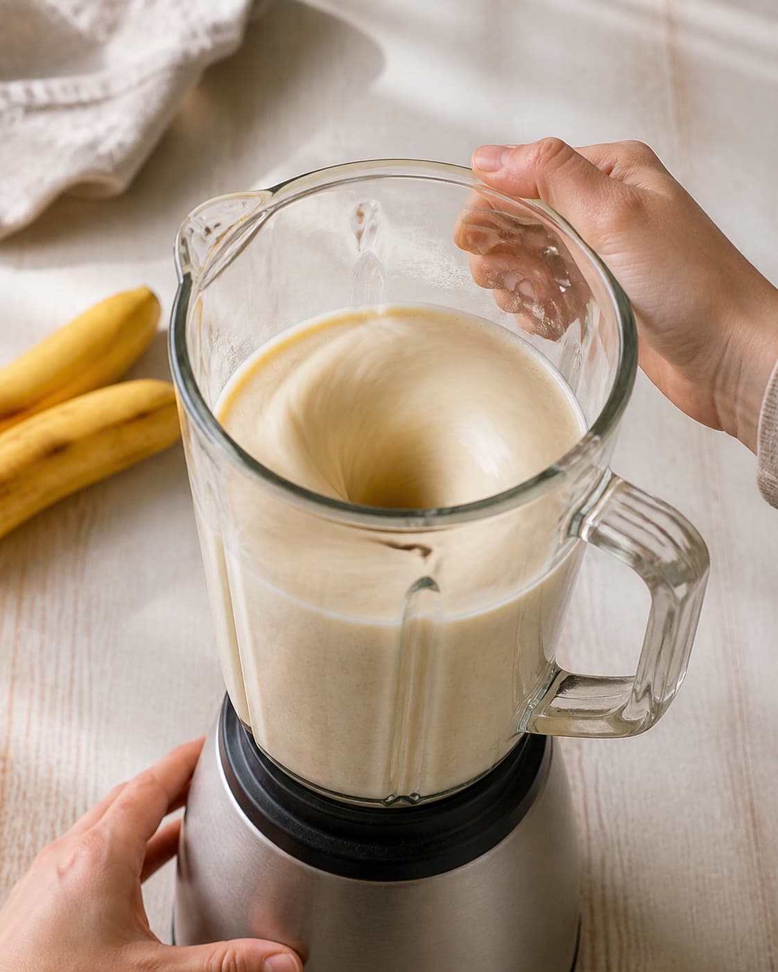 One single photorealistic instructional frame of a smooth pale base swirling inside one blender for Bananmilkshake med vaniljeis, featuring banan, vaniljeis, mælk, with only the named equipment and no unrelated food, text, logos or packaging under tilberedningen af bananmilkshake med vaniljeis