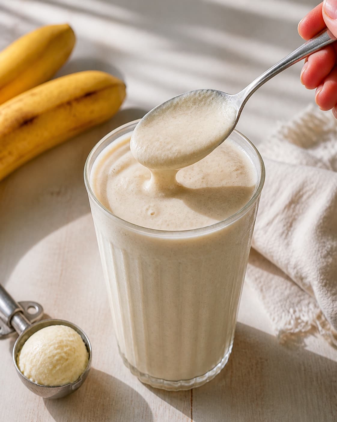 One single photorealistic instructional frame of one spoon checking the thick smoothie consistency for Bananmilkshake med vaniljeis, featuring banan, vaniljeis, mælk, with only the named equipment and no unrelated food, text, logos or packaging under tilberedningen af bananmilkshake med vaniljeis
