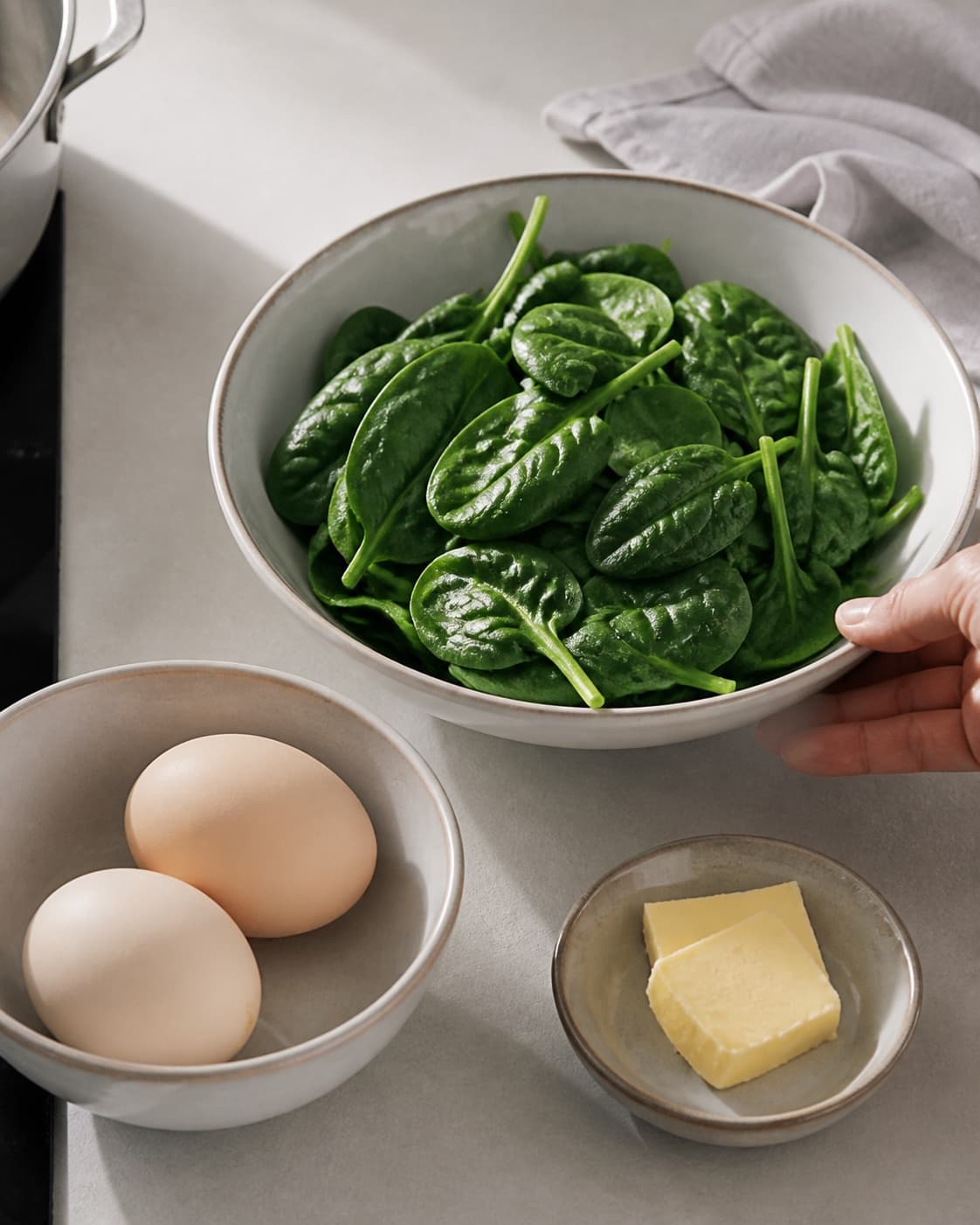 One single photorealistic instructional frame of prepared egg-dish fillings in separate bowls for Pocherede æg med spinat, featuring æg, babyspinat, smør, with only the named equipment and no unrelated food, text, logos or packaging under tilberedningen af pocherede æg med spinat