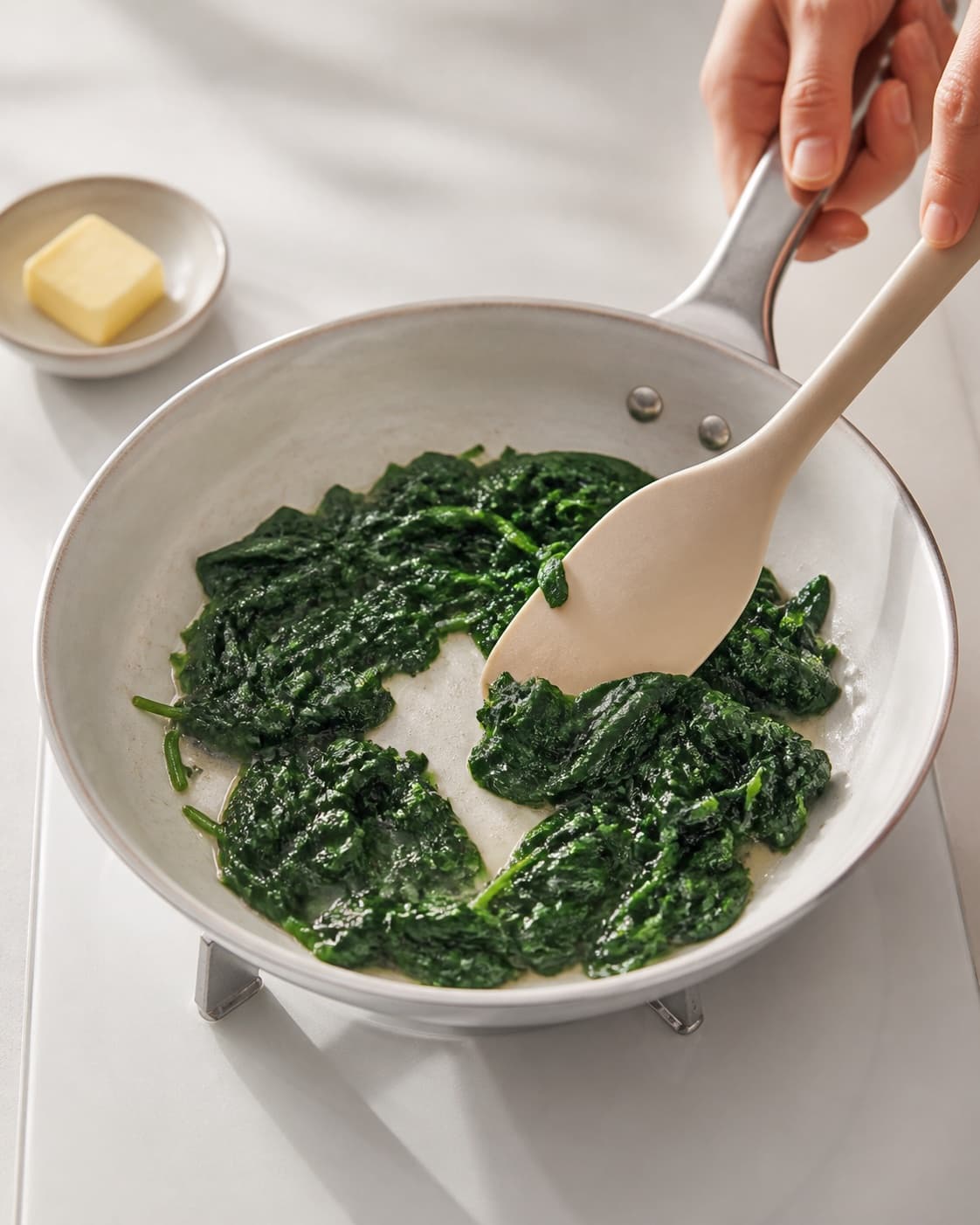 One single photorealistic instructional frame of the filling cooking until tender and dry in one skillet for Pocherede æg med spinat, featuring æg, babyspinat, smør, with only the named equipment and no unrelated food, text, logos or packaging under tilberedningen af pocherede æg med spinat