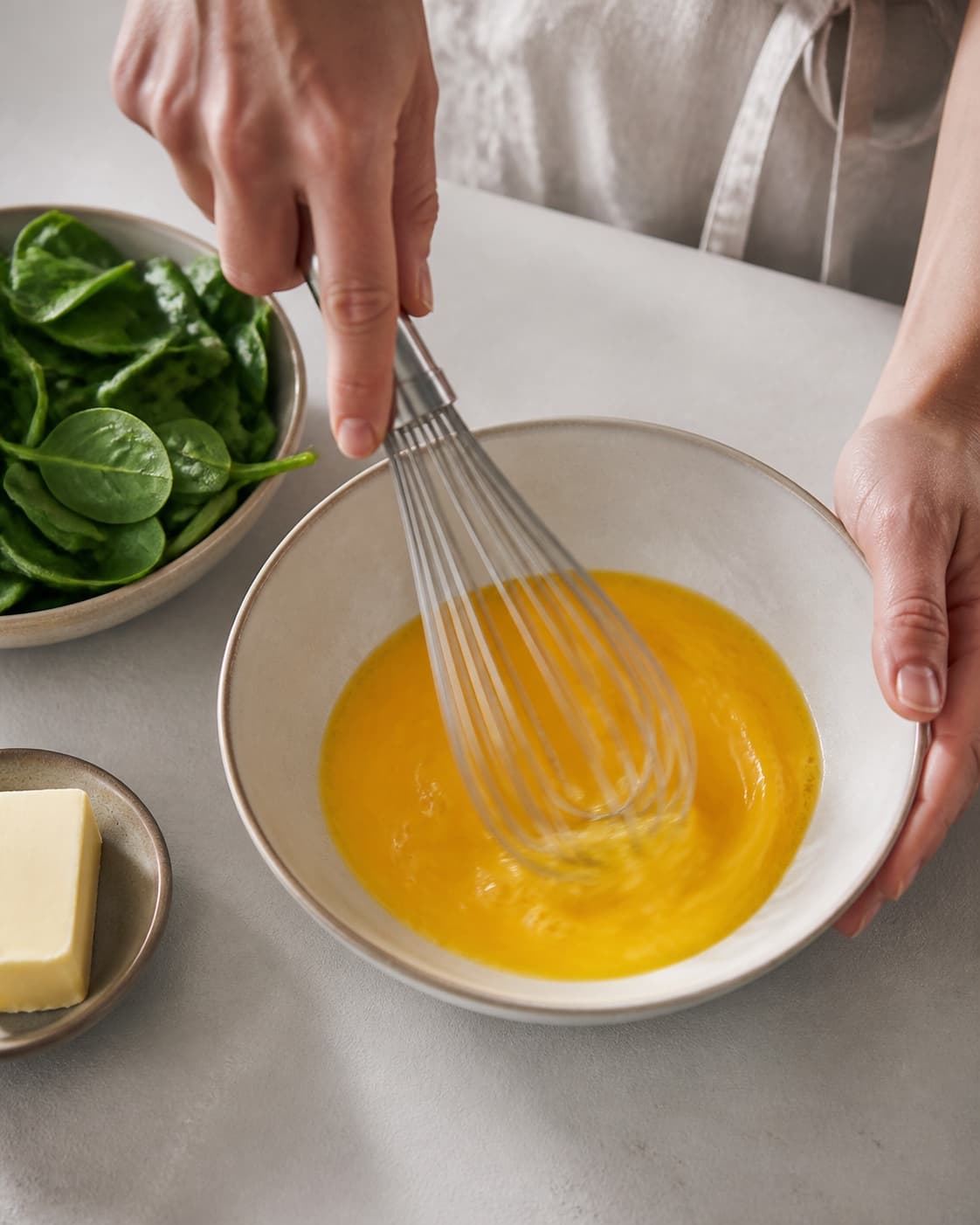 One single photorealistic instructional frame of eggs being whisked smoothly in one bowl for Pocherede æg med spinat, featuring æg, babyspinat, smør, with only the named equipment and no unrelated food, text, logos or packaging under tilberedningen af pocherede æg med spinat