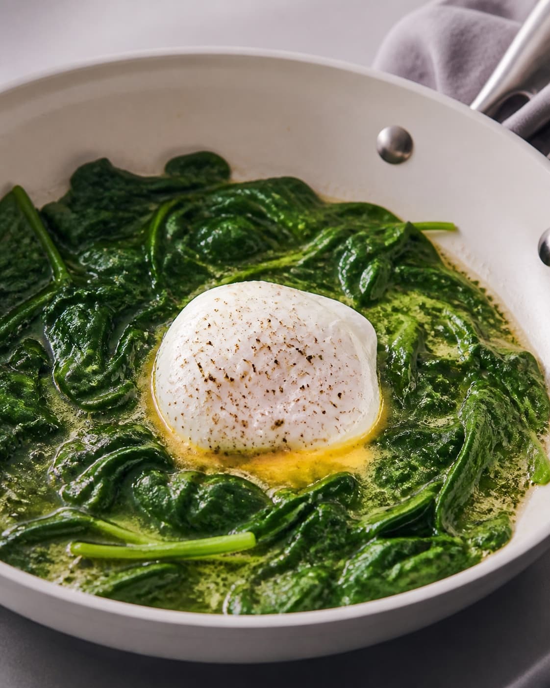 One single photorealistic instructional frame of the egg mixture gently setting around the filling for Pocherede æg med spinat, featuring æg, babyspinat, smør, with only the named equipment and no unrelated food, text, logos or packaging under tilberedningen af pocherede æg med spinat