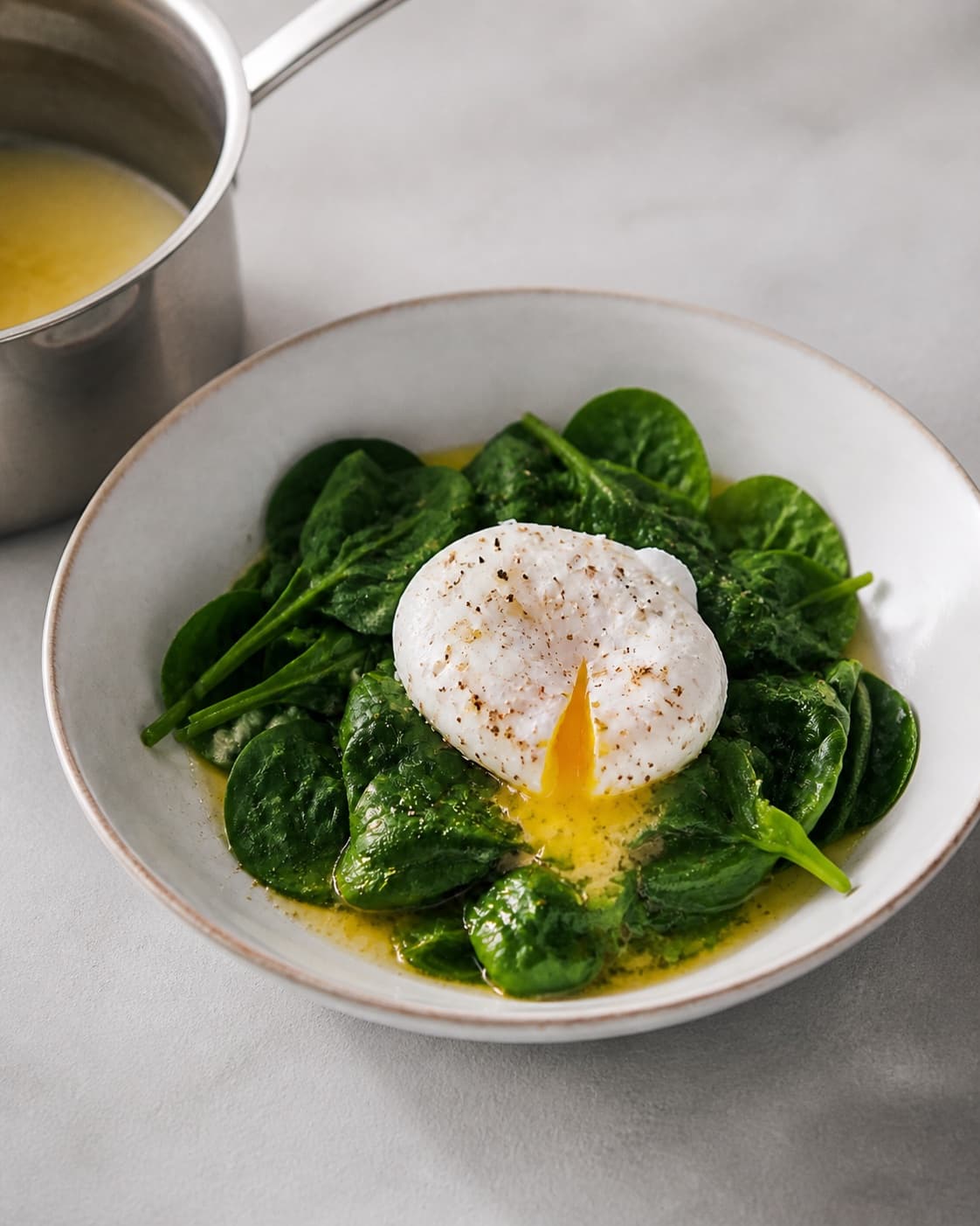 One single photorealistic instructional frame of the finished egg dish resting before serving for Pocherede æg med spinat, featuring æg, babyspinat, smør, with only the named equipment and no unrelated food, text, logos or packaging under tilberedningen af pocherede æg med spinat
