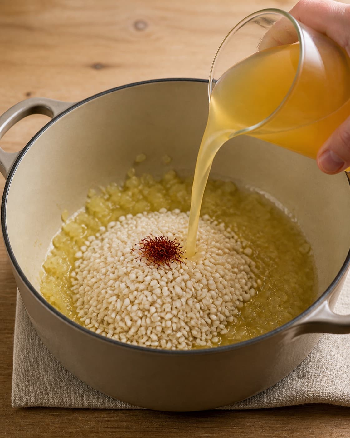One single photorealistic instructional frame of aromatic vegetables softening in the same heavy pot for Safranrisotto, featuring risottoris, safran, grøntsagsfond, with only the named equipment and no unrelated food, text, logos or packaging under tilberedningen af safranrisotto