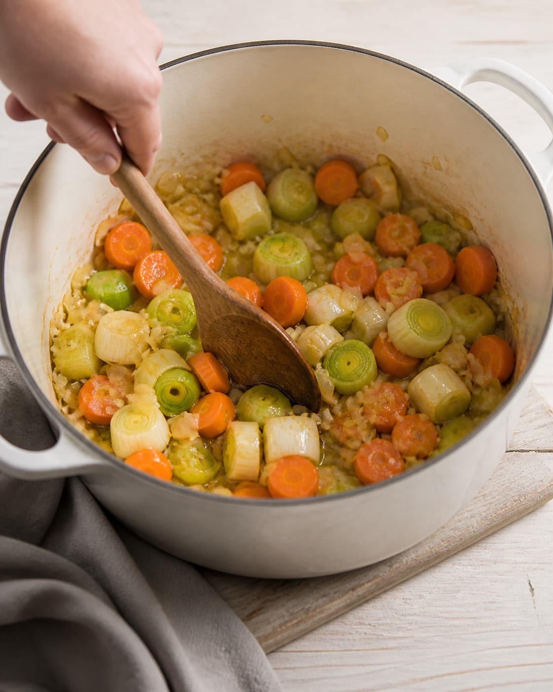 One single photorealistic instructional frame of aromatic vegetables softening in the same heavy pot for Grydestegt kylling og hjemmelavet kyllingefond - bouillion, featuring hel kylling, gulerødder, porrer, with only the named equipment and no unrelated food, text, logos or packaging under tilberedningen af grydestegt kylling og hjemmelavet kyllingefond - bouillion