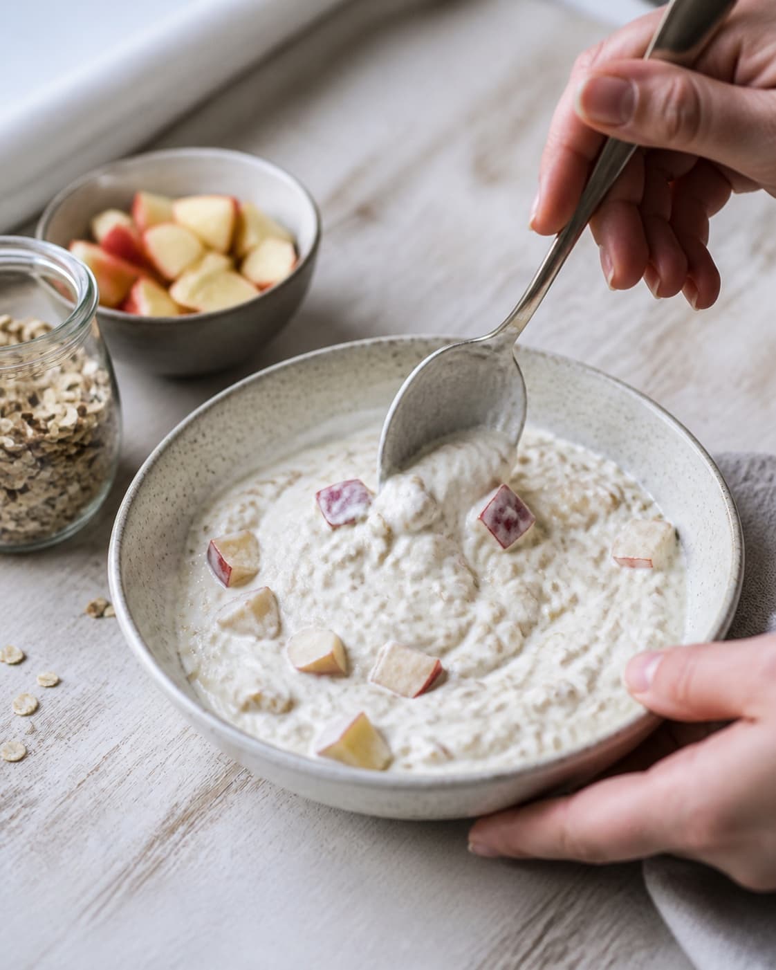 One single photorealistic instructional frame of the porridge consistency being adjusted with a spoon for Drænet yoghurt med knas og æbler, featuring græsk yoghurt, æbler, havregryn, with only the named equipment and no unrelated food, text, logos or packaging under tilberedningen af drænet yoghurt med knas og æbler