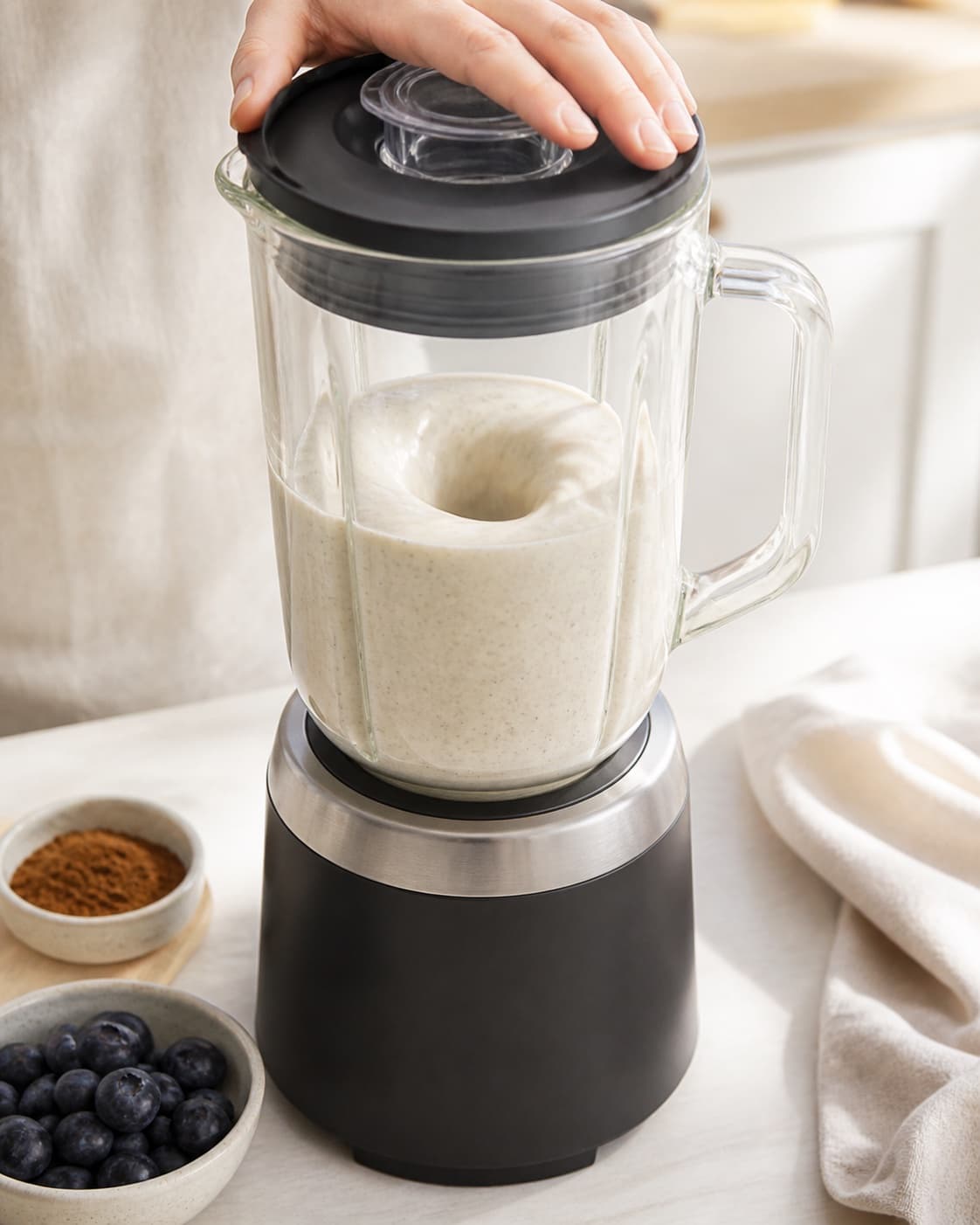 One single photorealistic instructional frame of a smooth pale base swirling inside one blender for Blåbær og lakridssmoothie, featuring blåbær, banan, lakridspulver, with only the named equipment and no unrelated food, text, logos or packaging under tilberedningen af blåbær og lakridssmoothie