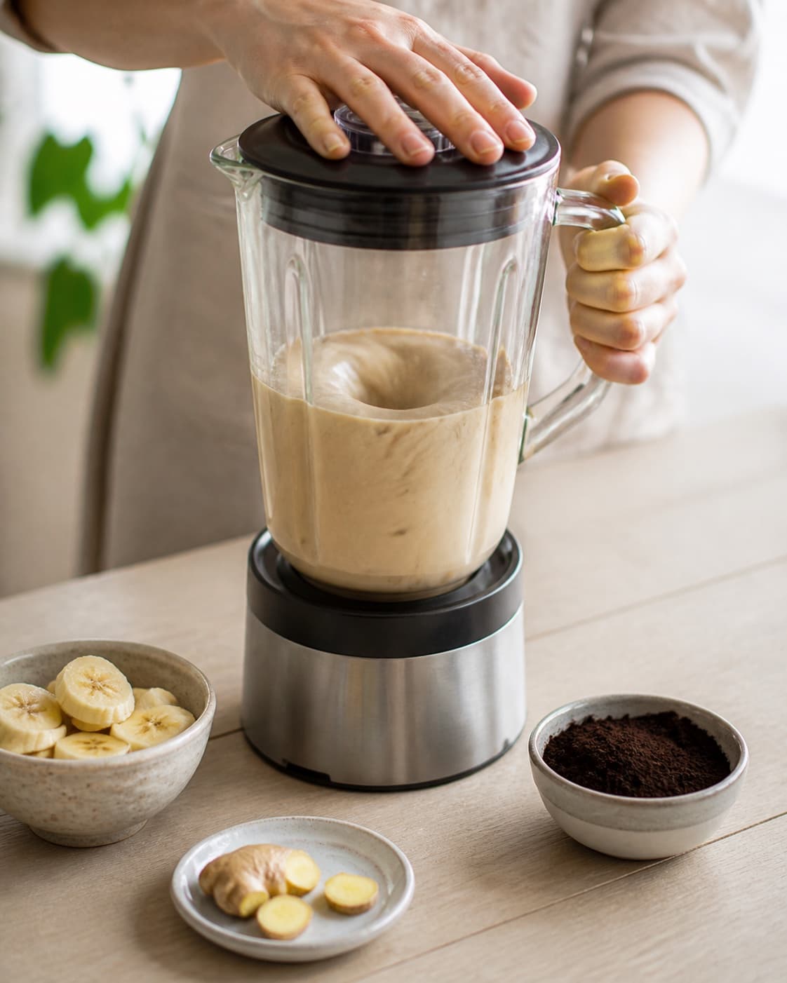 One single photorealistic instructional frame of a smooth pale base swirling inside one blender for Smoothie med ingefær og lakrids, featuring banan, frisk ingefær, lakridspulver, with only the named equipment and no unrelated food, text, logos or packaging under tilberedningen af smoothie med ingefær og lakrids