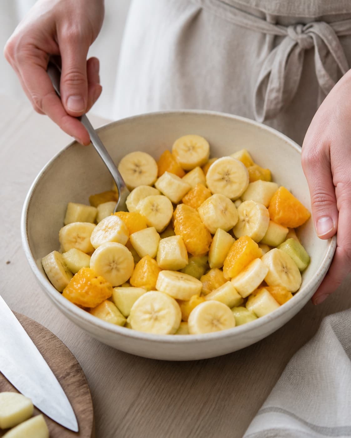 Fresh apple pear banana and orange being cut and gently tossed in one bowl, no oven, roasting tray or cooked fruit under tilberedningen af frugtsalat med chokolade