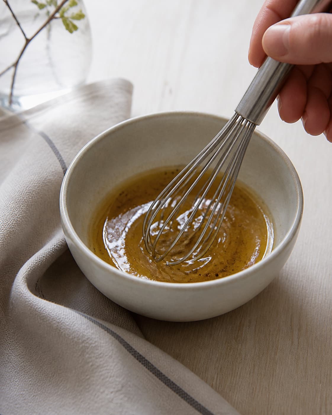 One single photorealistic instructional frame of a glossy dressing being whisked in one small bowl for Frugtsalat med chokolade, featuring æbler, pærer, banan, with only the named equipment and no unrelated food, text, logos or packaging under tilberedningen af frugtsalat med chokolade