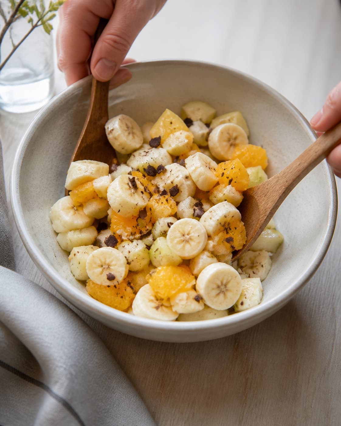 One single photorealistic instructional frame of the prepared salad components being gently tossed together for Frugtsalat med chokolade, featuring æbler, pærer, banan, with only the named equipment and no unrelated food, text, logos or packaging under tilberedningen af frugtsalat med chokolade