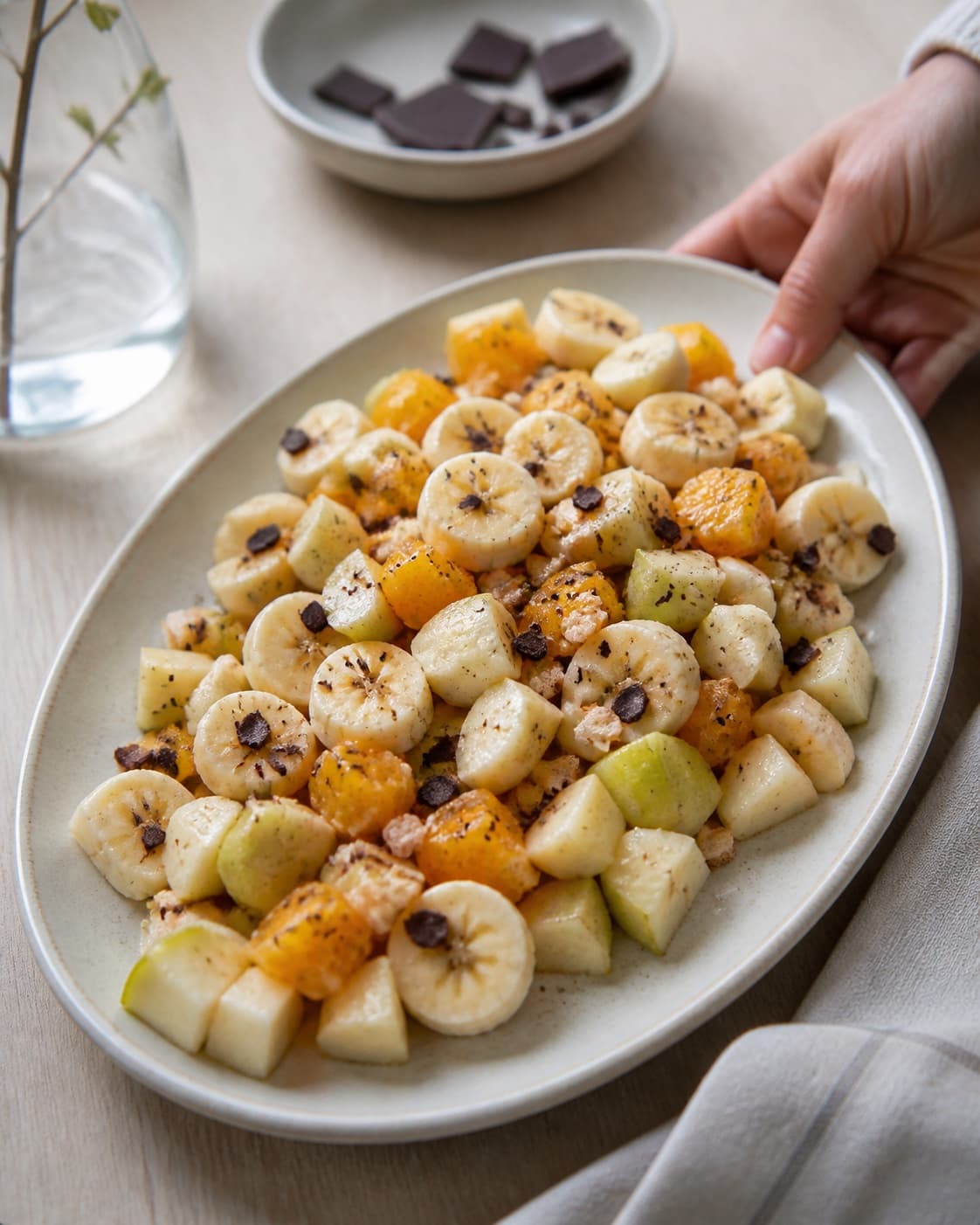 One single photorealistic instructional frame of the finished salad arranged loosely on one serving platter for Frugtsalat med chokolade, featuring æbler, pærer, banan, with only the named equipment and no unrelated food, text, logos or packaging under tilberedningen af frugtsalat med chokolade