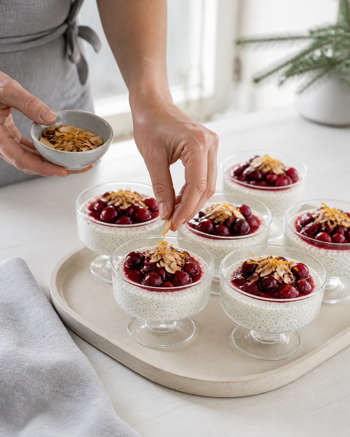 En hånd topper seks kolde glas chia à la mande med afgrænset kirsebærkompot, ristede mandelflager og appelsinskal