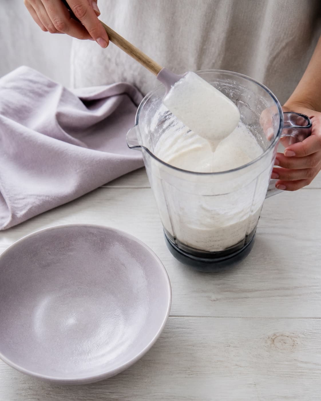 En hånd viser den glatte let skummende hytteostbase med mælk, skyr, vanilje og citron på en dejskraber i blenderen