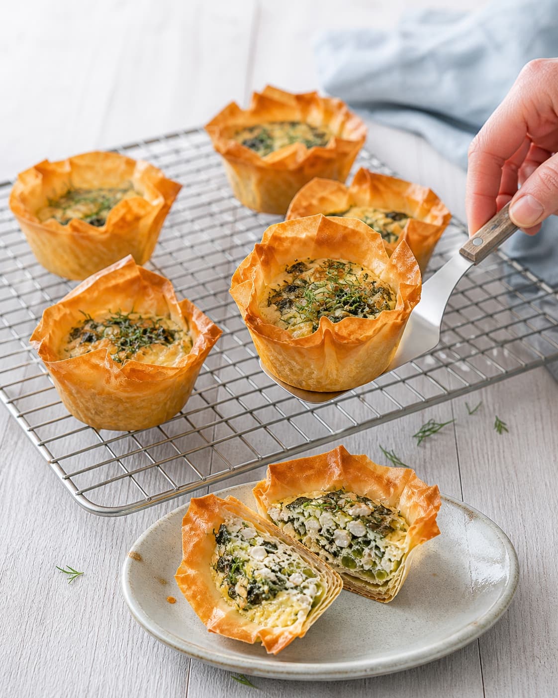 En tynd palet løfter en gylden filomuffin fra risten, mens en overskåret muffin viser fast spinatfyld og sprød lagdelt bund