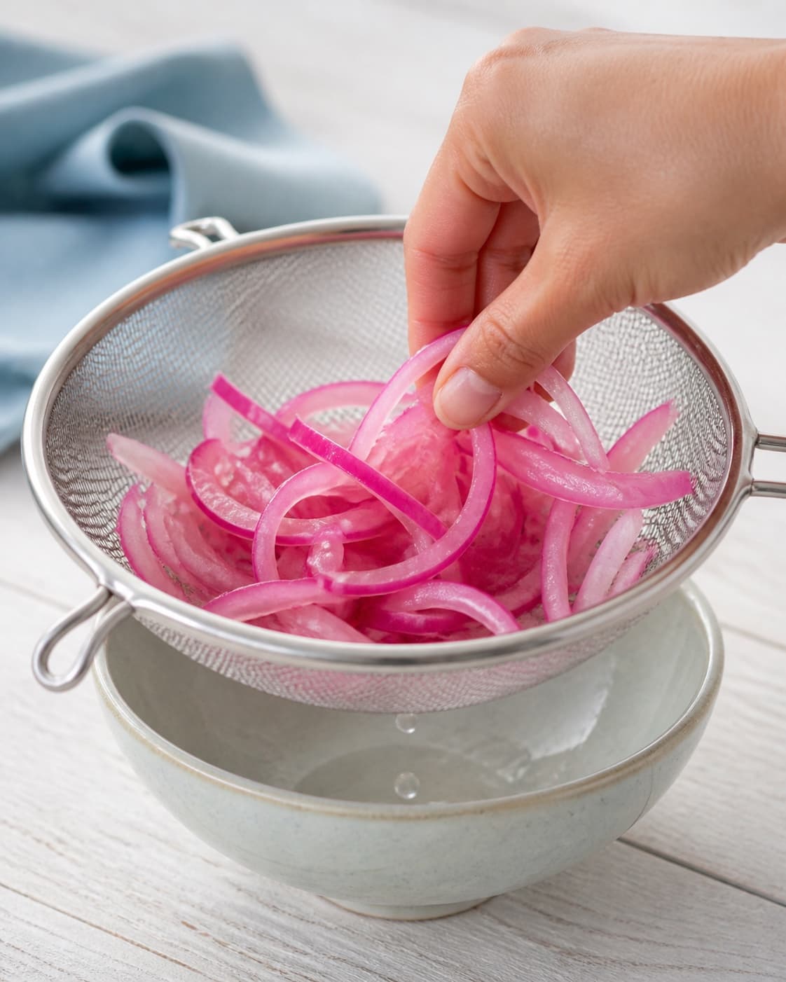 En hånd løfter de bløde pink rødløgsstrimler i en fin si, mens den sidste klare syltelage drypper ned i skålen