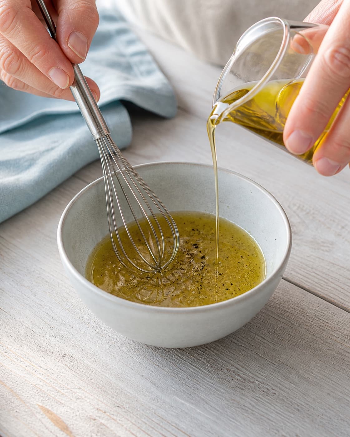 Olivenolie hældes i en tynd stråle under piskning af lime, honning og sort peber til en let blank dressing uden salt